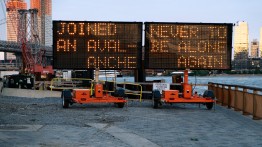 Two construction signs spell out installation title Joined an Avalanche, Never to be Alone Again