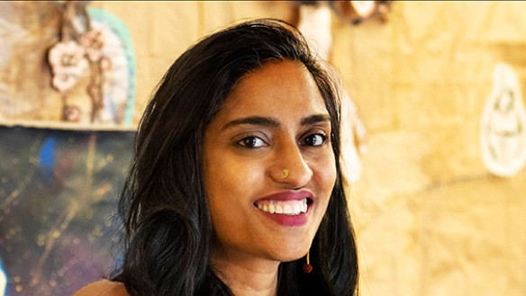 Portrait of Chitra Ganesh seated in front of one of her works